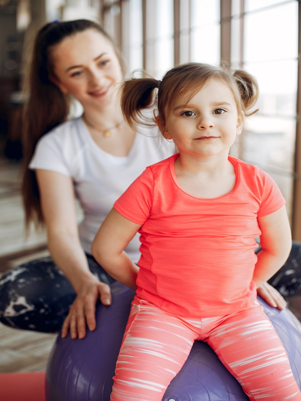 Woman in a sportswear. Mother with little daughter. Family are engaged in gymnastics in a gym