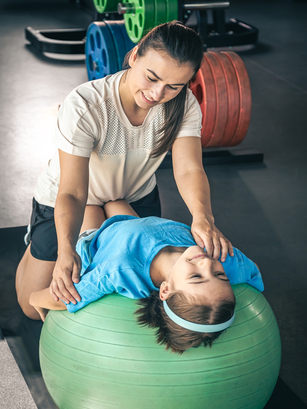 Little sporty girl and young beautiful mother doing stretching with fitness ball at gym.